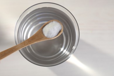 Photo of Spoon with baking soda over glass of water on light background, top view. Space for text