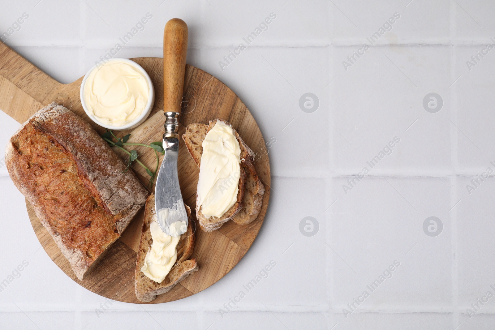 Photo of Tasty bread with butter and knife on white tiled table, top view. Space for text