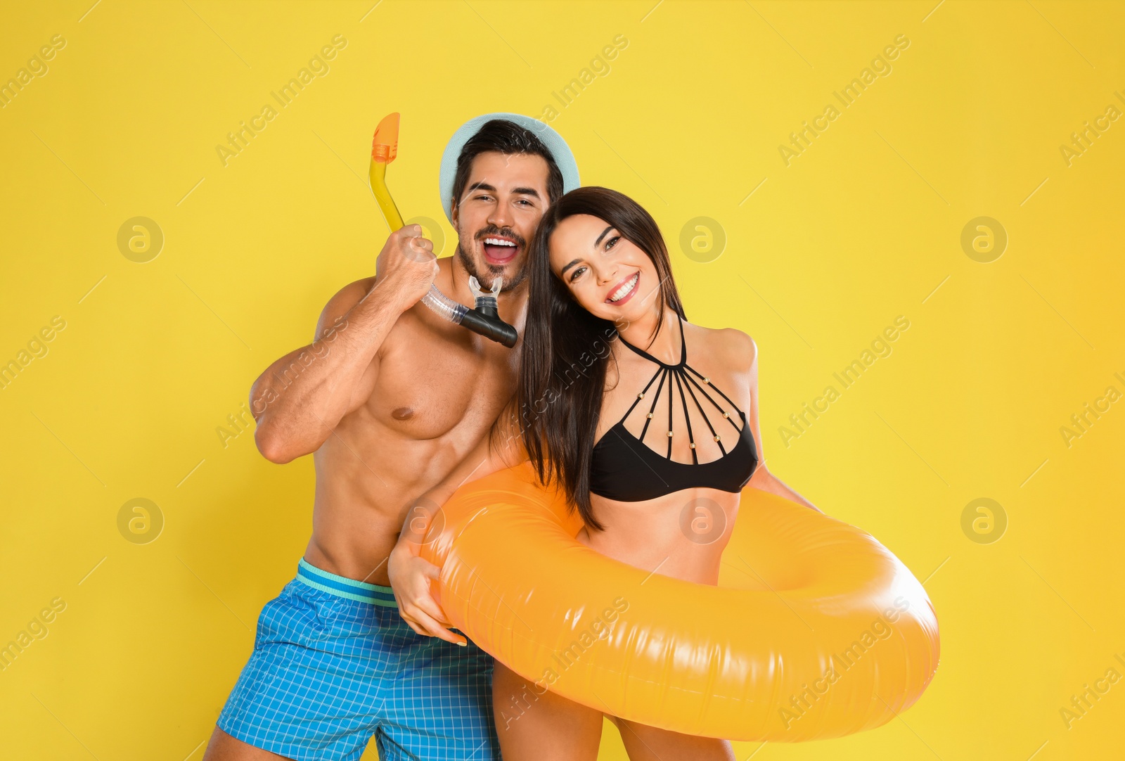 Photo of Young attractive couple in beachwear with snorkel and inflatable ring on yellow background