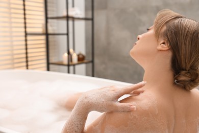 Beautiful woman taking bath with foam in tub indoors. Space for text