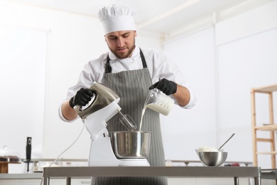 Male pastry chef preparing dough in mixer at kitchen table
