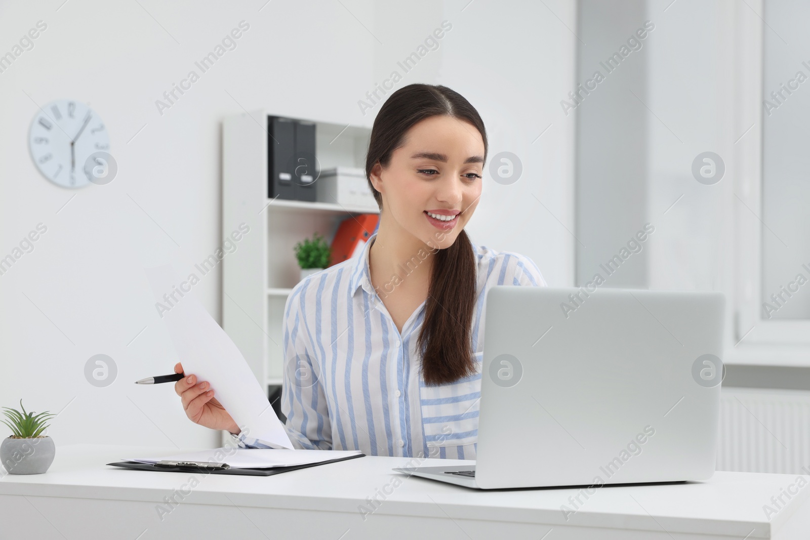 Photo of Young female intern working with laptop at table in office