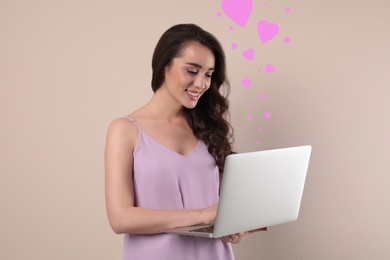 Young woman visiting dating site via laptop on beige background