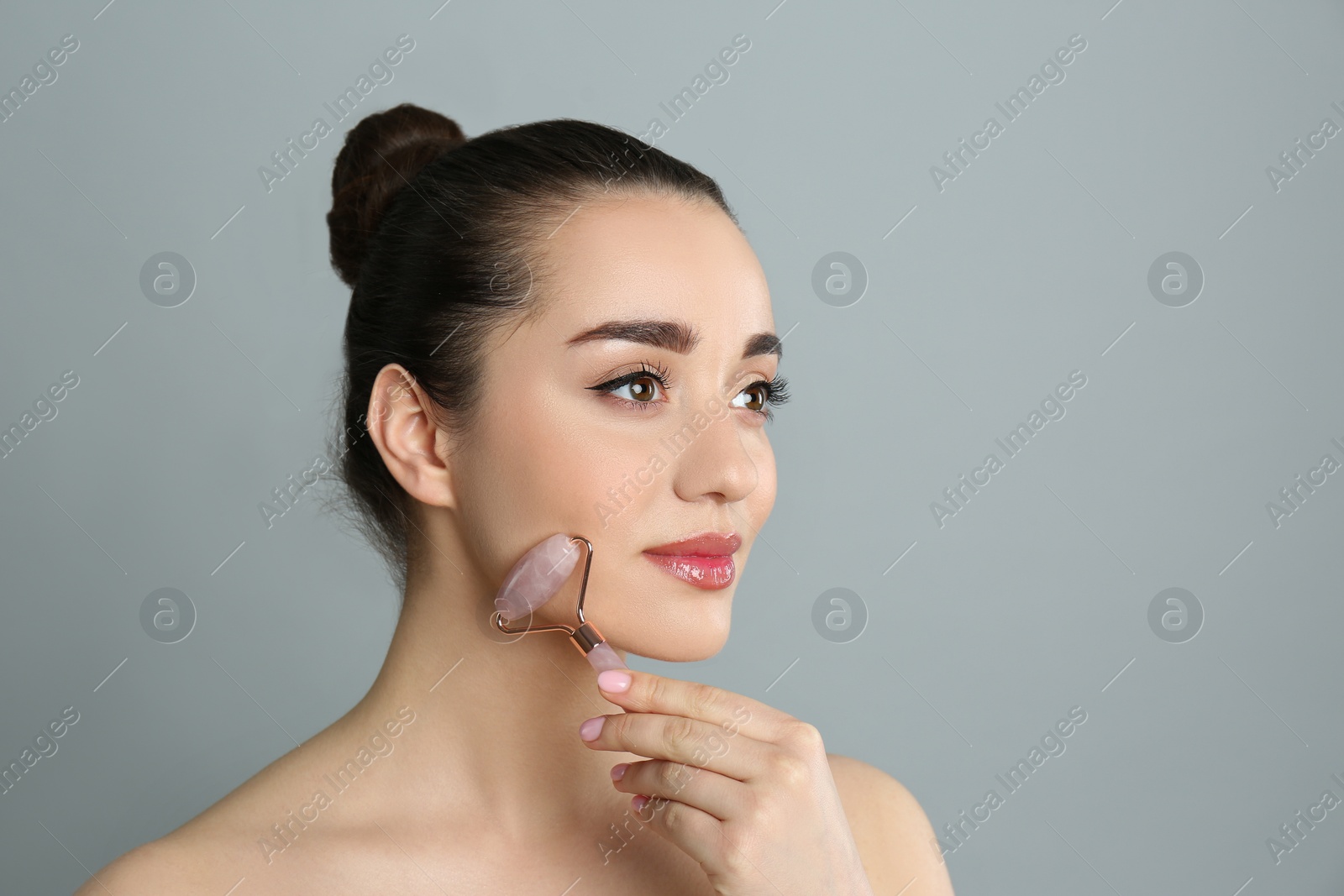 Photo of Woman using natural pink quartz face roller on grey background, space for text