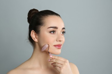 Photo of Woman using natural pink quartz face roller on grey background, space for text