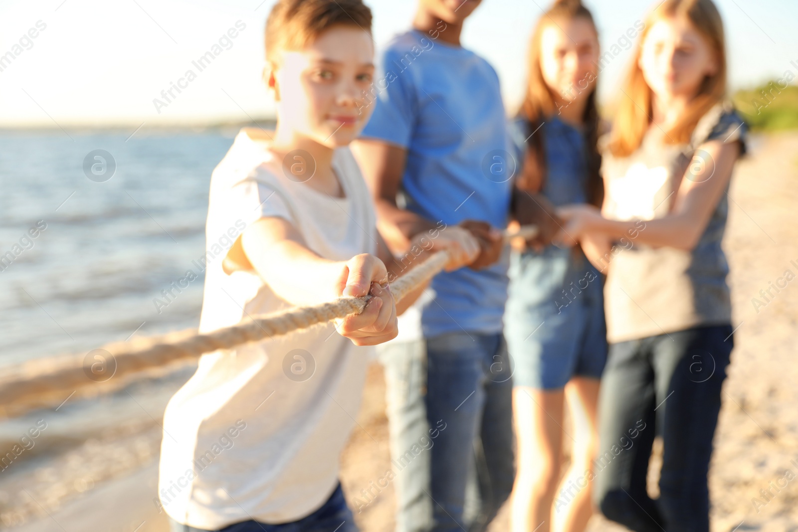 Photo of Group of children pulling rope during tug of war game on beach. Summer camp