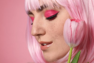 Beautiful woman with bright makeup, fake freckles and tulip on pink background, closeup