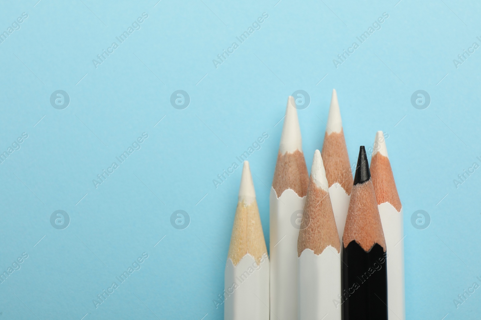 Photo of Black and white pencils on light blue background, flat lay with space for text. Racism concept