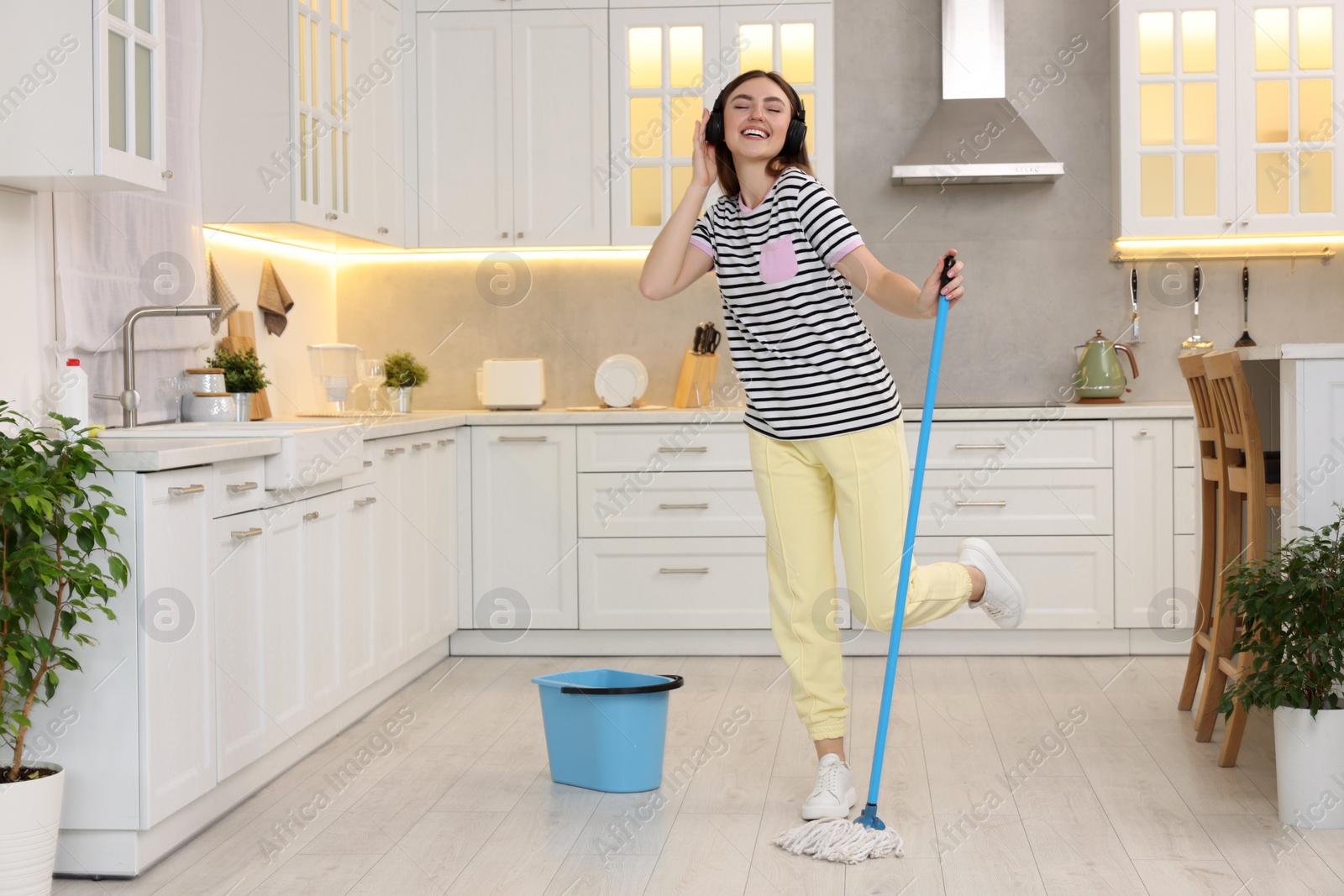 Photo of Enjoying cleaning. Woman in headphones listening music and mopping in kitchen