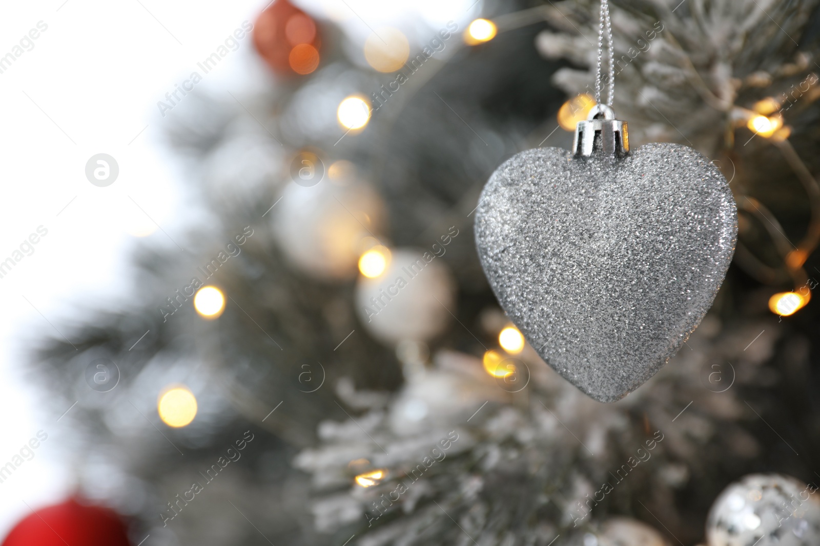 Photo of Beautiful heart shaped holiday bauble hanging on Christmas tree, closeup. Space for text