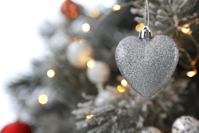 Beautiful heart shaped holiday bauble hanging on Christmas tree, closeup. Space for text