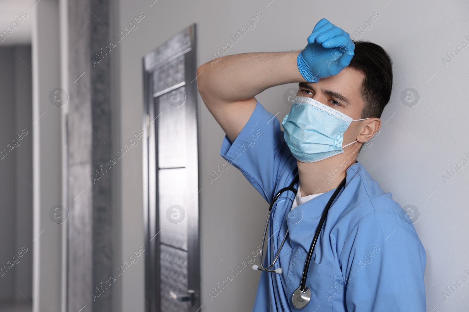 Photo of Exhausted doctor near grey wall in hospital, space for text