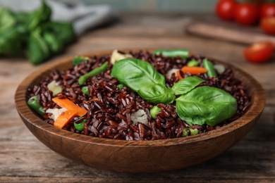 Photo of Plate of brown rice with vegetables on wooden table, closeup