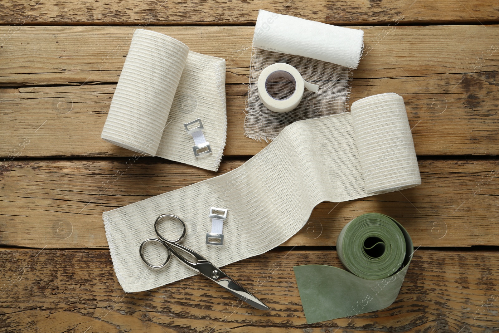 Photo of Medical bandage rolls, sticking plaster and scissors on wooden background, flat lay