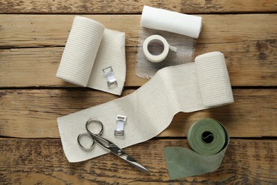 Photo of Medical bandage rolls, sticking plaster and scissors on wooden background, flat lay