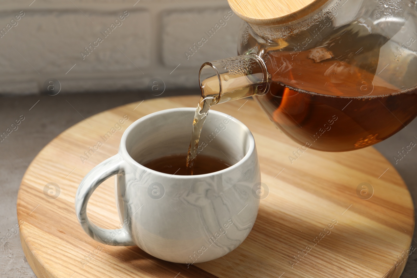 Photo of Pouring aromatic tea in cup at table, closeup