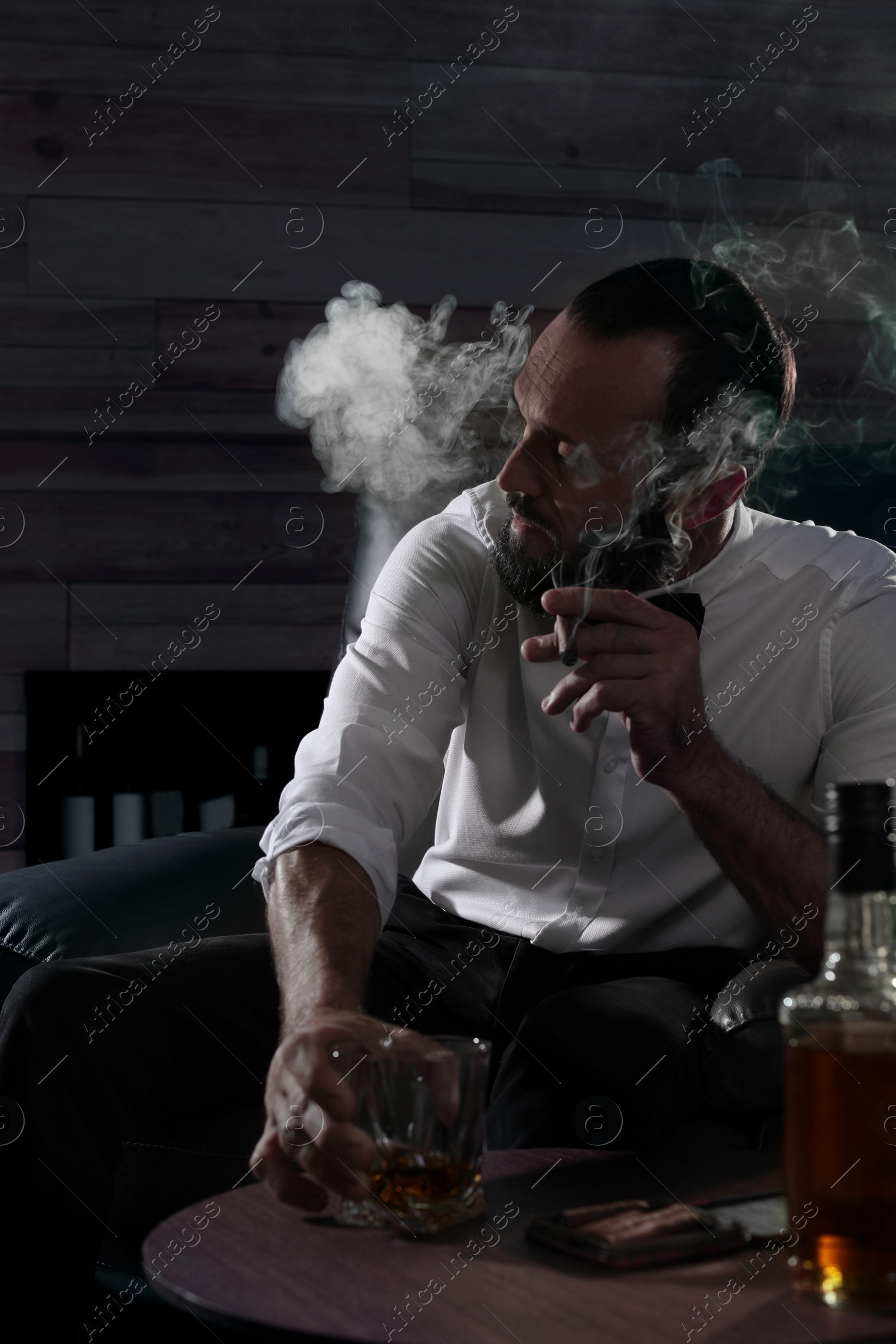 Photo of Man with glass of whiskey and cigar sitting at table indoors