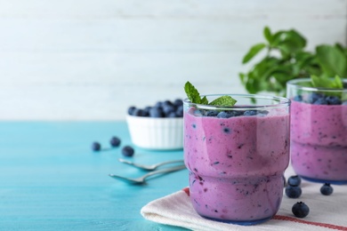 Glasses of tasty blueberry smoothie and fabric on light blue wooden table, space for text