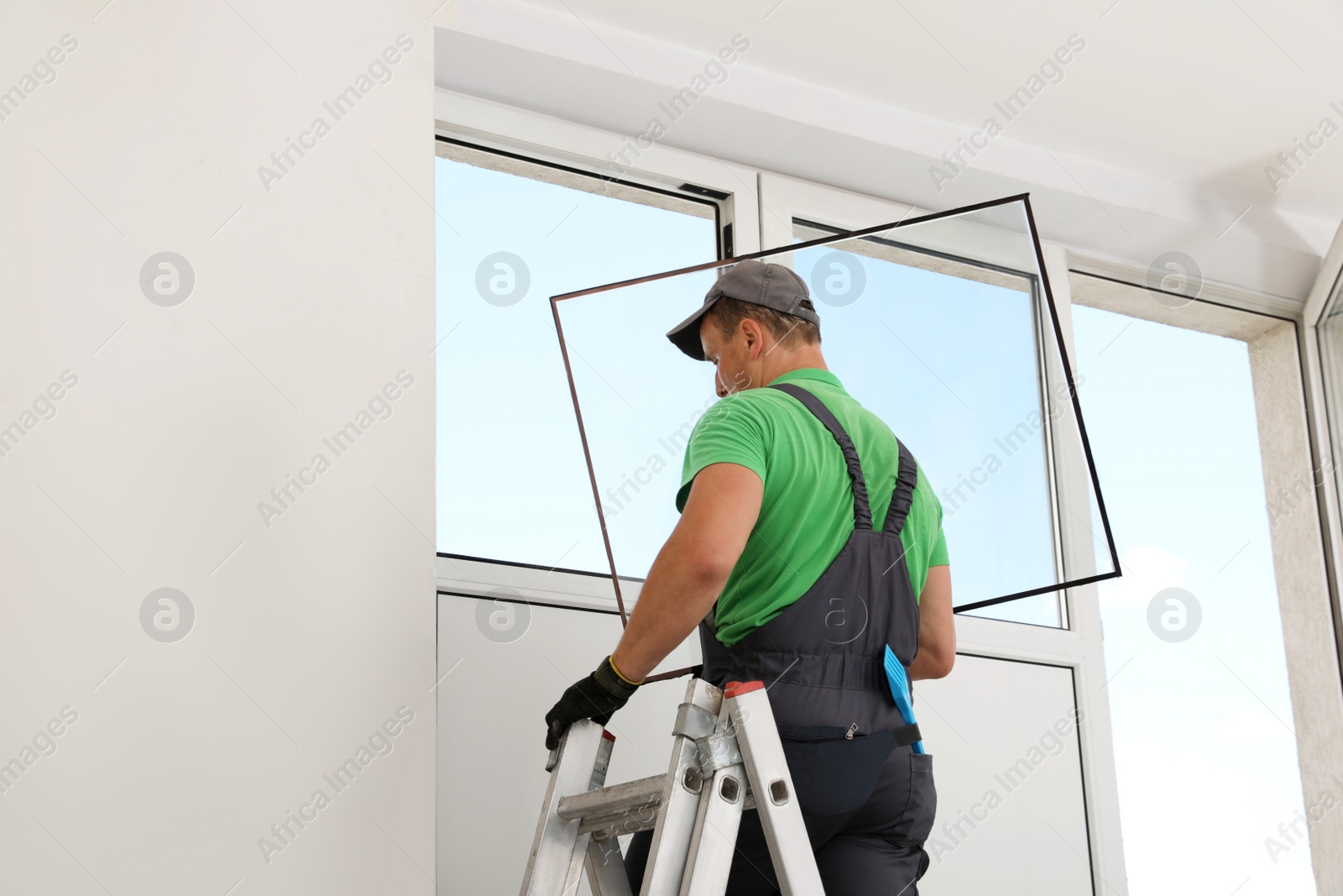 Photo of Worker on folding ladder installing window indoors