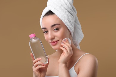 Photo of Beautiful woman in terry towel removing makeup with cotton pad on beige background