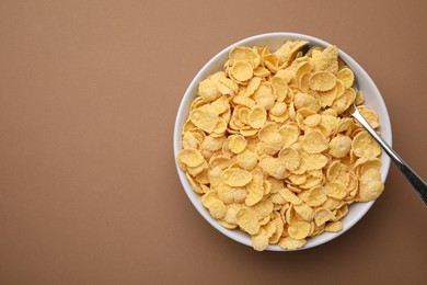 Breakfast cereal. Tasty corn flakes in bowl and spoon on brown table, top view. Space for text