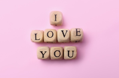 Photo of Phrase I Love You made of wooden cubes on pink background, flat lay