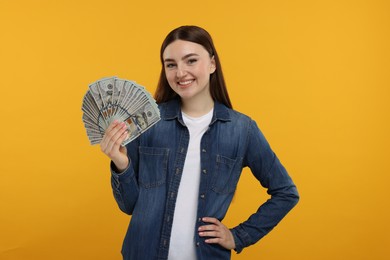 Happy woman with dollar banknotes on orange background