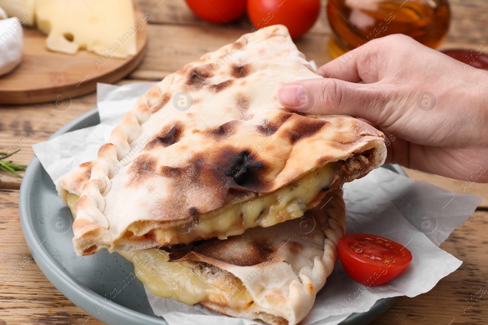 Photo of Woman holding tasty pizza calzone with cheese at wooden table, closeup