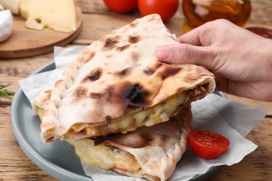 Woman holding tasty pizza calzone with cheese at wooden table, closeup