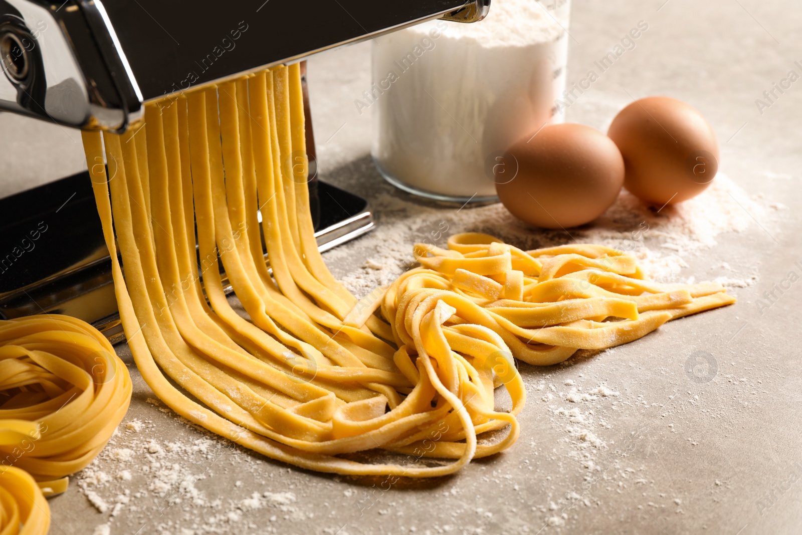 Photo of Pasta maker machine with dough and products on grey table