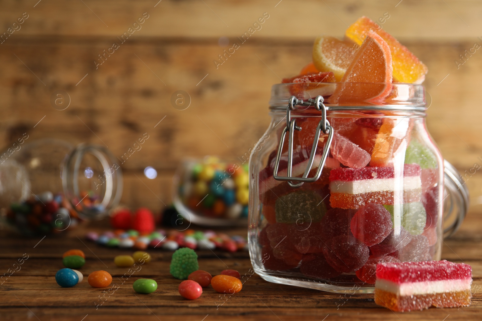 Photo of Delicious jelly candies in jar on wooden table, closeup. Space for text