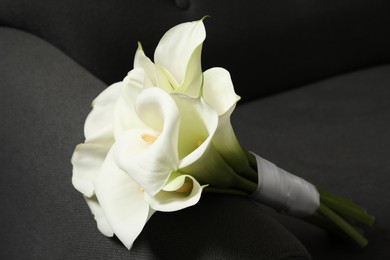 Photo of Beautiful calla lily flowers tied with ribbon on sofa, closeup