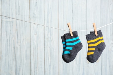 Baby socks on laundry line against wooden background, space for text. Child accessories