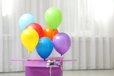 Gift box with bright air balloons indoors. Space for text