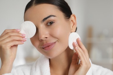 Beautiful woman removing makeup with cotton pads indoors, closeup