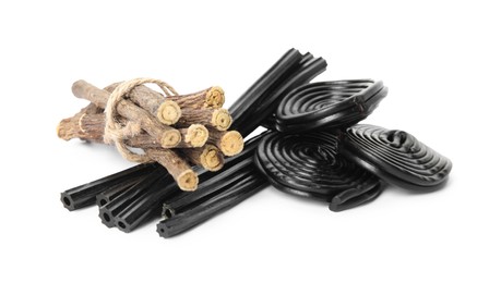 Photo of Tasty black candies and dried sticks of liquorice root on white background