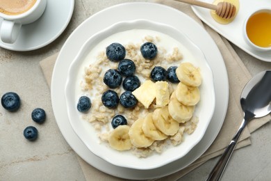 Tasty oatmeal with banana, blueberries, butter and milk served in bowl on light grey table, flat lay