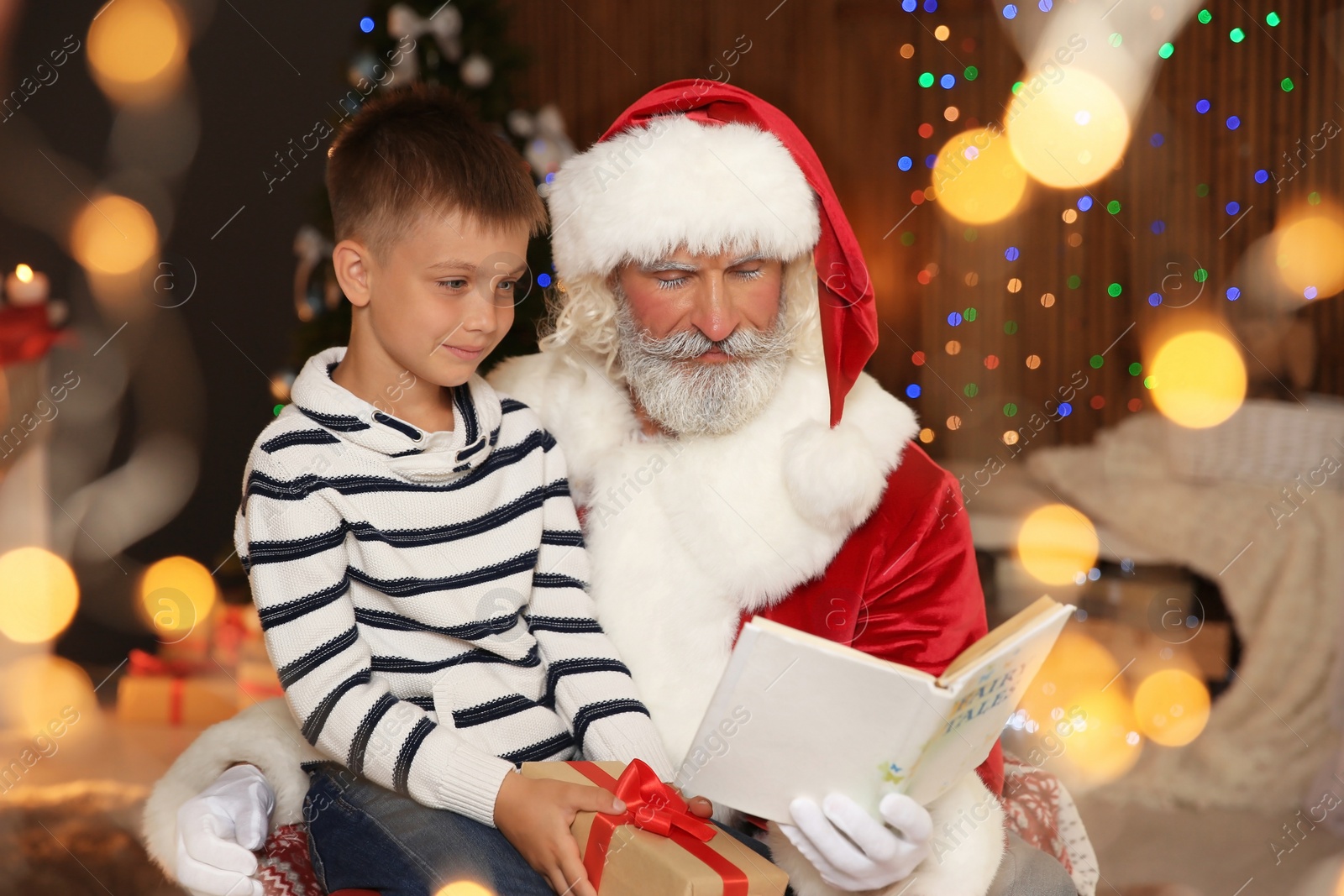 Photo of Little child with Santa Claus reading Christmas story at home