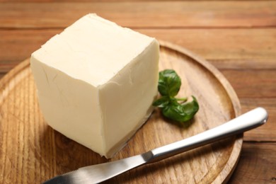 Photo of Block of tasty butter, knife and basil on wooden table, closeup