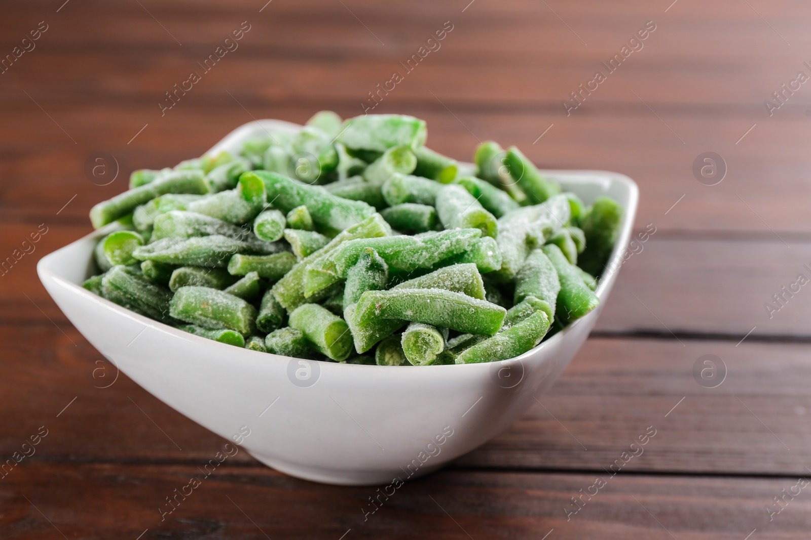 Photo of Frozen cut green beans on wooden table, closeup. Vegetable preservation