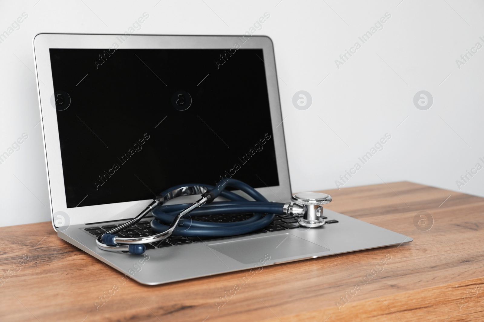 Photo of Laptop with blank screen and stethoscope on table against light background. Computer repair