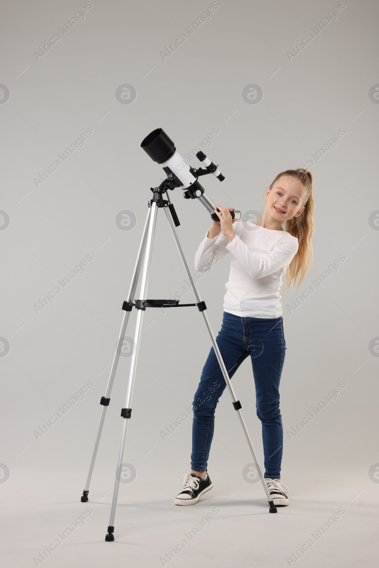 Photo of Happy little girl with telescope on light grey background