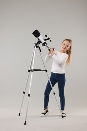 Happy little girl with telescope on light grey background