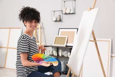 Young woman mixing paints on palette with brush near easel in studio