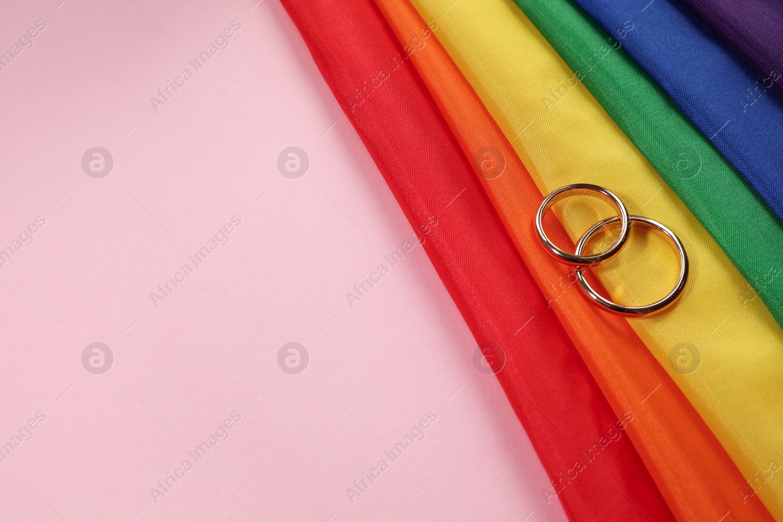 Photo of Rainbow LGBT flag and wedding rings on pink background. Space for text