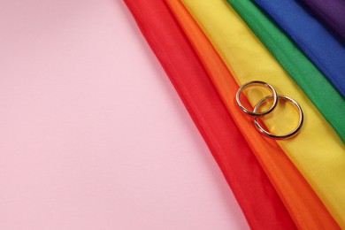 Rainbow LGBT flag and wedding rings on pink background. Space for text