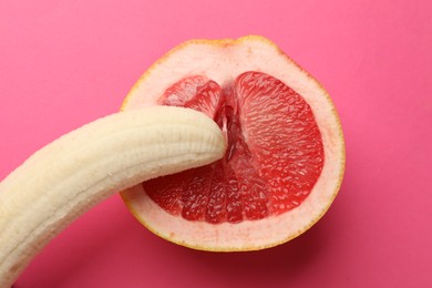 Photo of Banana and half of grapefruit on pink background, top view. Sex concept