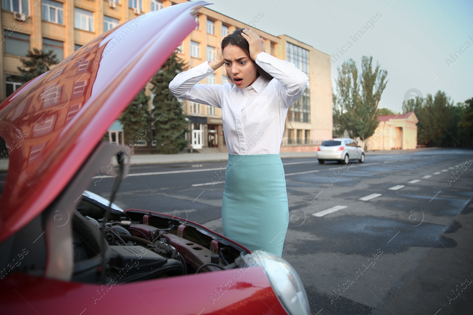 Photo of Stressed woman standing near broken car on city street