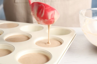 Pouring batter into cupcake tray at white table in kitchen, closeup