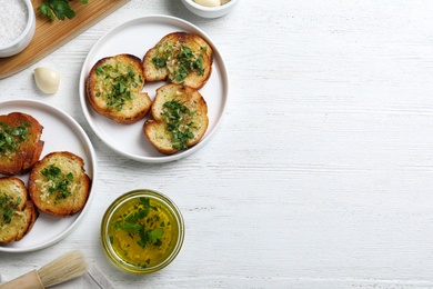 Slices of toasted bread with garlic and herb on white wooden table, flat lay. Space for text